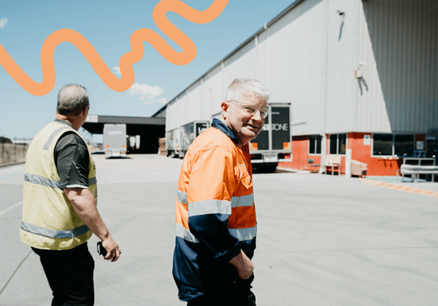Two men in high vis at distribution centre, one smiling to camera